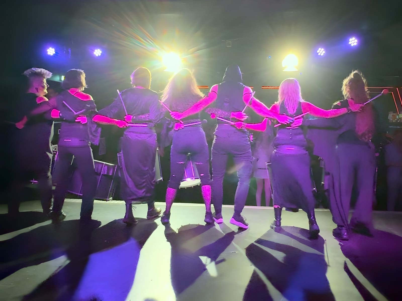 Die Band von hinten auf der Bühne des U4, die Arme ineinander gehakt, vor sich Scheinwerfer in Violett und Gold.